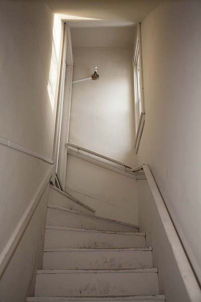 20" x 30" Archival Inkjet Print. Color photograph. Claustrophobic stairway, beige interior, one window and door, light reflecting, dirty