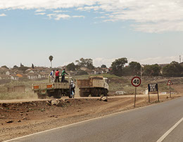 Three men riding on the back of a dirt truck in Nairobi, Kenya